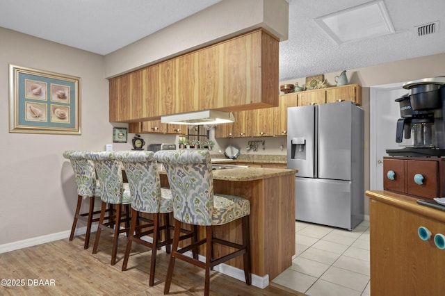 kitchen with light stone counters, stainless steel refrigerator with ice dispenser, ventilation hood, kitchen peninsula, and a breakfast bar