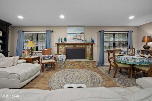 living room with a stone fireplace, plenty of natural light, a textured ceiling, and hardwood / wood-style flooring