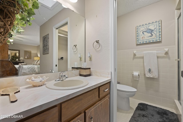 bathroom featuring vanity, toilet, a textured ceiling, and tile walls