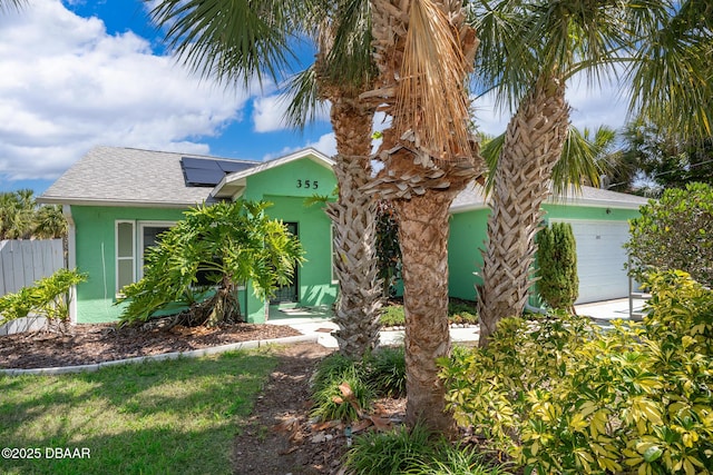 355 Palm Cir, Flagler Beach, FL 32136 - view of front facade featuring stucco siding, a garage, roof mounted solar panels, and roof with shingles