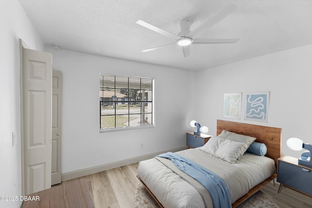 bedroom with a textured ceiling, a ceiling fan, baseboards, and wood finished floors