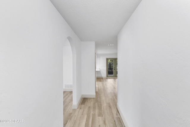 hall featuring visible vents, baseboards, light wood-type flooring, arched walkways, and a textured ceiling