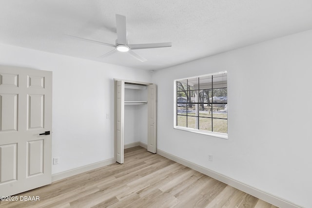 unfurnished bedroom with light wood finished floors, a closet, a textured ceiling, and baseboards