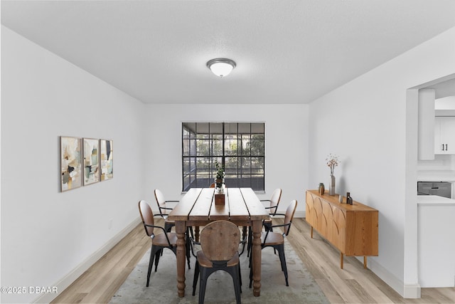 dining area featuring baseboards, a textured ceiling, and light wood-style floors