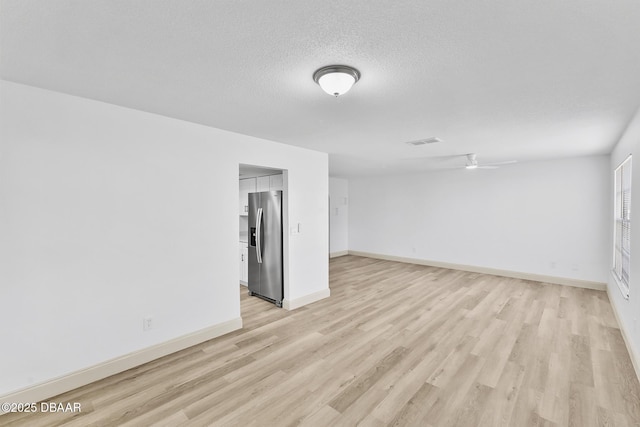 spare room featuring light wood-type flooring, baseboards, a textured ceiling, and visible vents