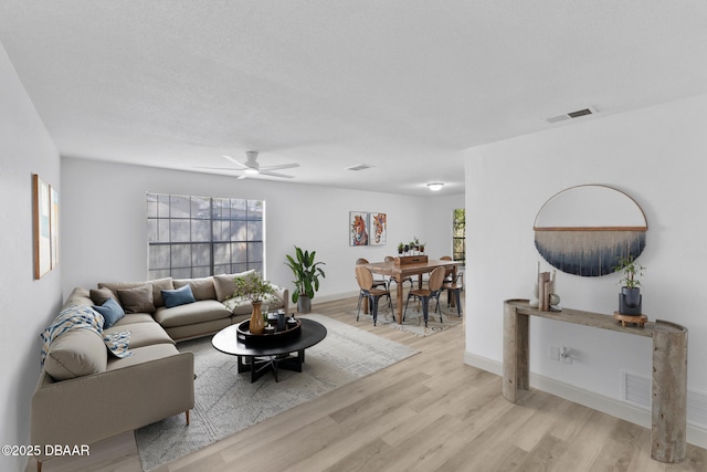 living room with ceiling fan, baseboards, visible vents, and light wood-type flooring