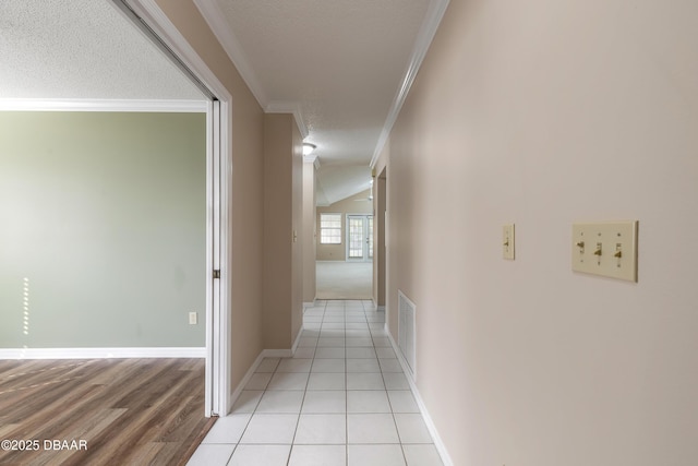 hall featuring light tile patterned flooring, ornamental molding, vaulted ceiling, and a textured ceiling