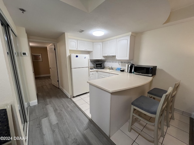 kitchen featuring kitchen peninsula, white refrigerator, light hardwood / wood-style floors, white cabinetry, and a breakfast bar area