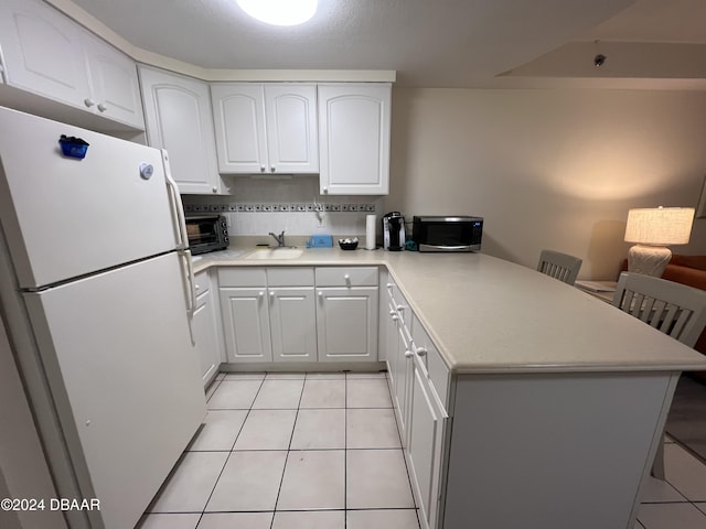 kitchen with white fridge, kitchen peninsula, a breakfast bar area, and white cabinetry