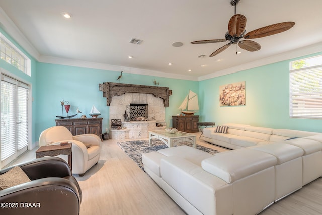 living room with a fireplace, light hardwood / wood-style flooring, ceiling fan, and crown molding