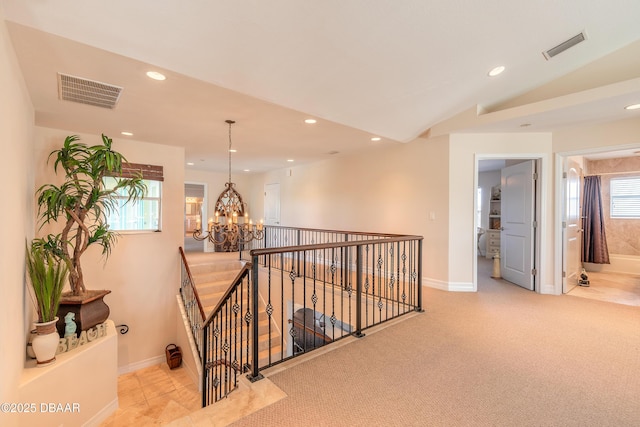 hall with vaulted ceiling, light colored carpet, and an inviting chandelier