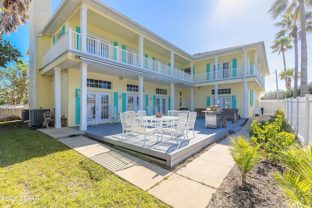 rear view of property featuring a lawn, a patio area, a balcony, and french doors