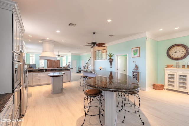 kitchen with custom exhaust hood, ceiling fan, light wood-type flooring, and a breakfast bar area