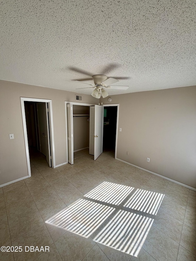 unfurnished bedroom featuring light tile patterned floors, visible vents, ceiling fan, a textured ceiling, and baseboards