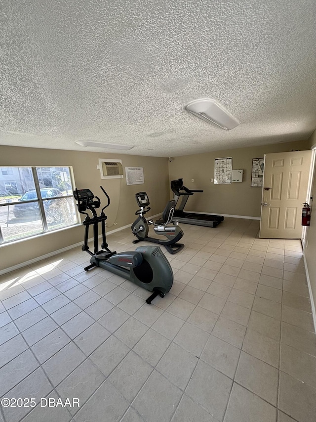 workout area featuring light tile patterned flooring, a wall unit AC, a textured ceiling, and baseboards