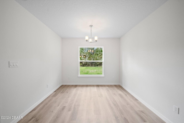 spare room with light hardwood / wood-style flooring, a notable chandelier, and a textured ceiling