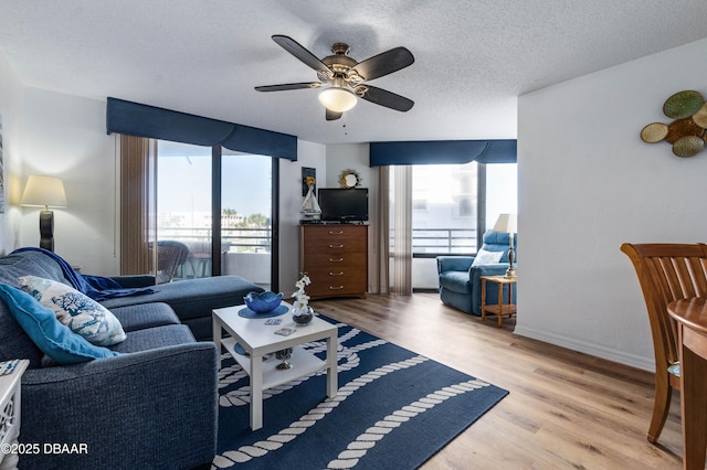 living room featuring a textured ceiling, light wood finished floors, a ceiling fan, and baseboards