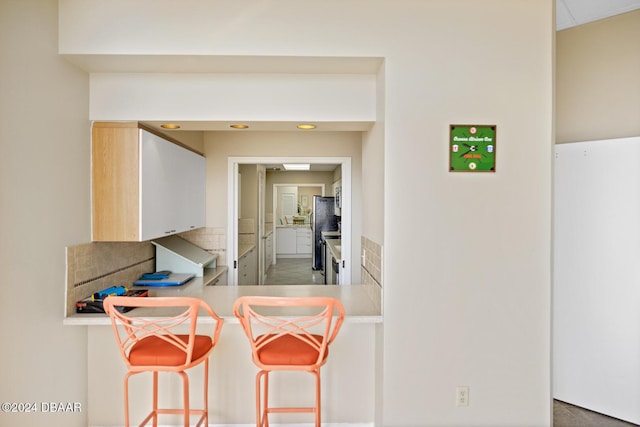 kitchen with a breakfast bar area, light countertops, decorative backsplash, freestanding refrigerator, and a peninsula