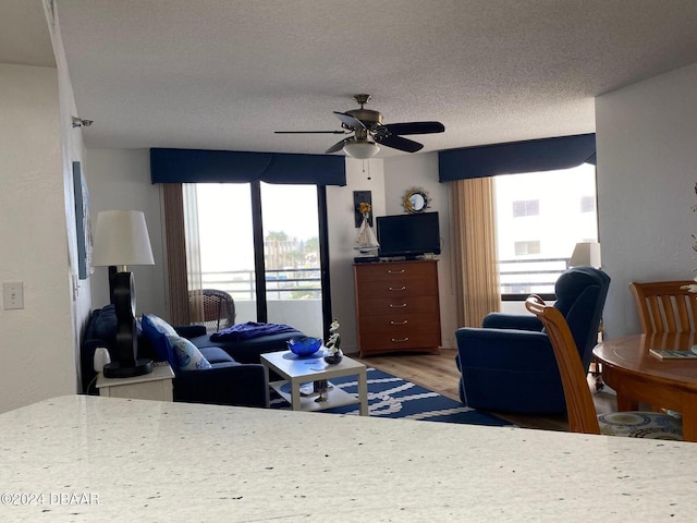 living area with ceiling fan, a textured ceiling, and wood finished floors