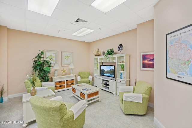 living area featuring light tile patterned floors, a drop ceiling, visible vents, and baseboards