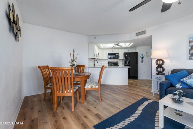 dining room with ceiling fan, a textured ceiling, visible vents, baseboards, and light wood finished floors