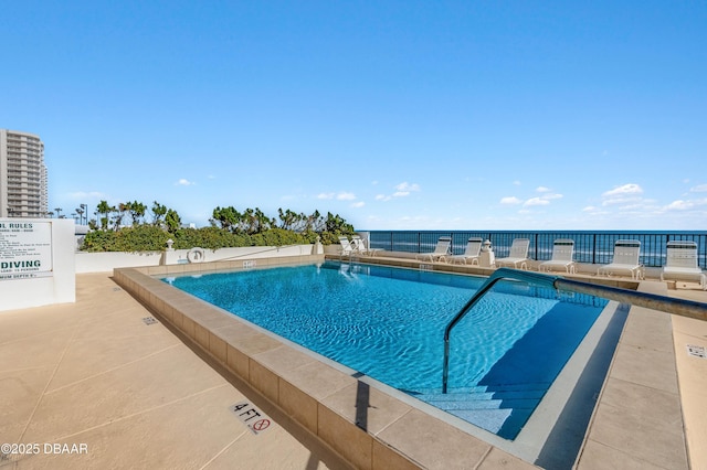 pool with a water view, fence, and a patio