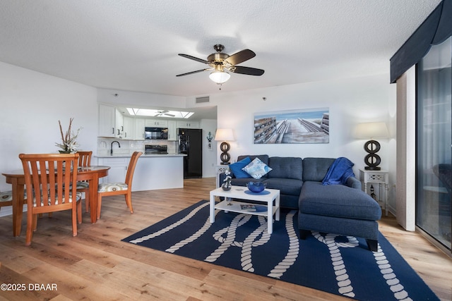 living area with light wood-type flooring, a textured ceiling, and a ceiling fan