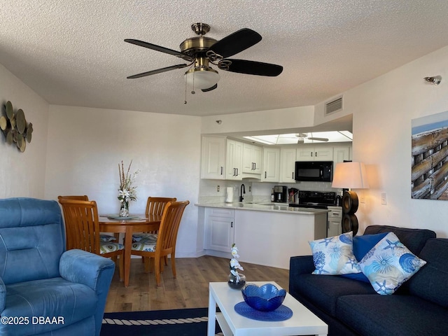 living room with dark wood-style flooring, visible vents, ceiling fan, and a textured ceiling