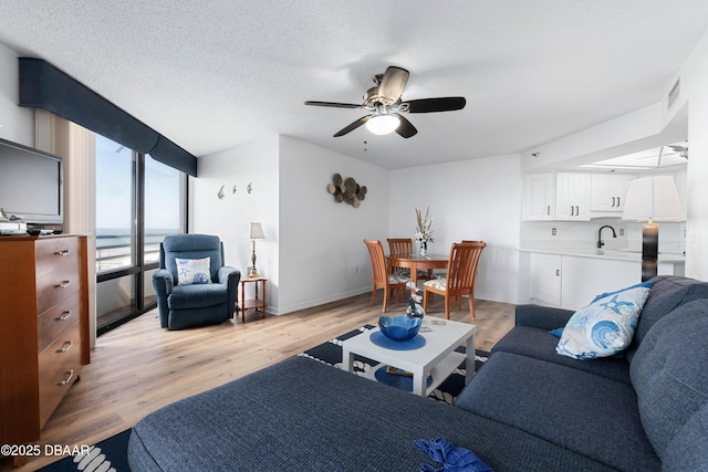 living area with a textured ceiling, ceiling fan, visible vents, baseboards, and light wood-style floors