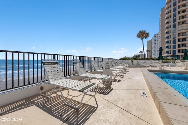 view of patio / terrace featuring a water view, a view of the beach, and a community pool