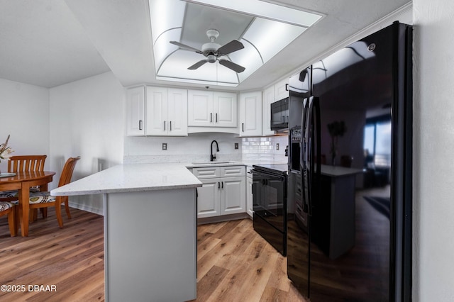 kitchen with a peninsula, a sink, white cabinets, black appliances, and a tray ceiling