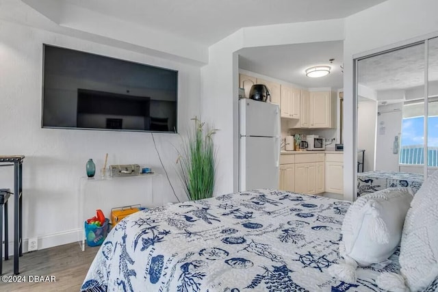 bedroom with hardwood / wood-style floors, white fridge, and connected bathroom