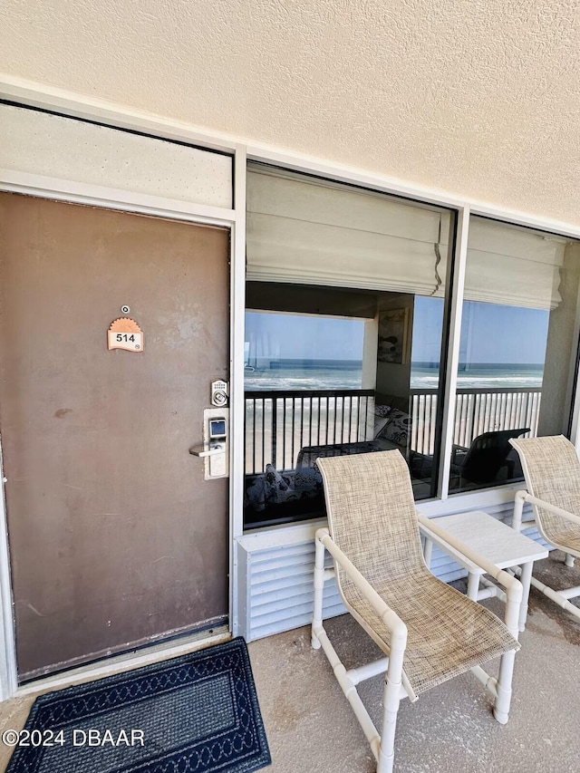 property entrance with a balcony, a water view, and a view of the beach