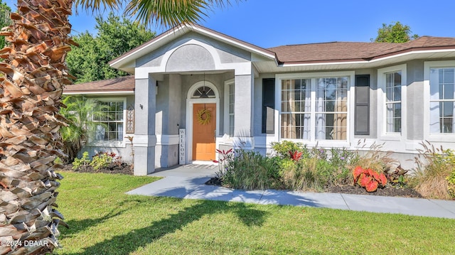 view of front of home with stucco siding, a shingled roof, and a front yard