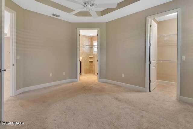 unfurnished bedroom featuring light carpet, connected bathroom, a spacious closet, and ceiling fan