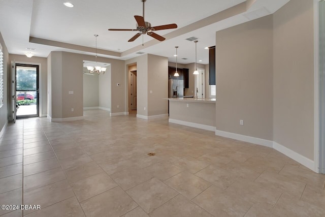 unfurnished living room featuring ceiling fan with notable chandelier and a tray ceiling