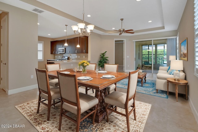 dining area featuring ceiling fan with notable chandelier and a tray ceiling