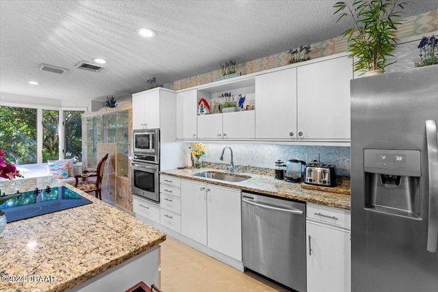 kitchen featuring light stone counters, stainless steel appliances, a textured ceiling, sink, and white cabinets