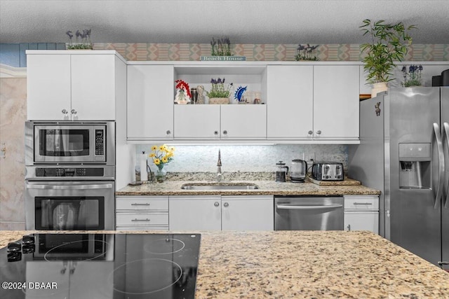 kitchen featuring stainless steel appliances, white cabinetry, a textured ceiling, light stone countertops, and sink