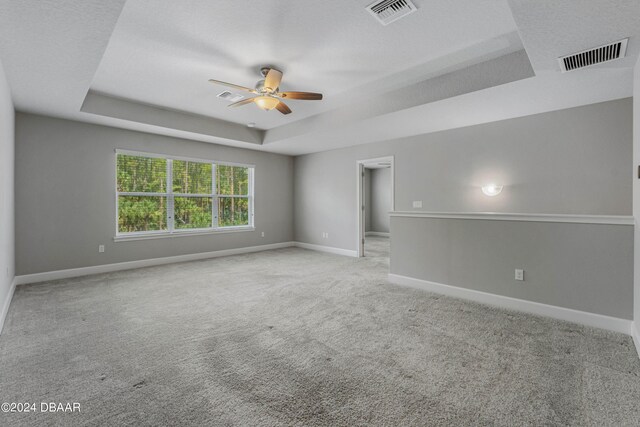 carpeted empty room with a textured ceiling, ceiling fan, and a raised ceiling