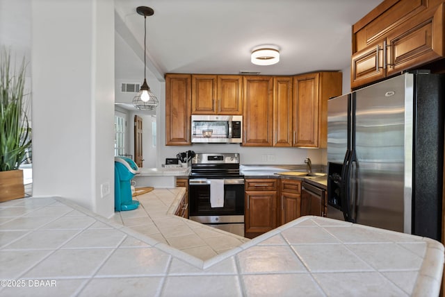 326 Flushing Ave, Daytona Beach, FL 32118 - kitchen featuring appliances with stainless steel finishes, tile countertops, brown cabinetry, a sink, and hanging light fixtures