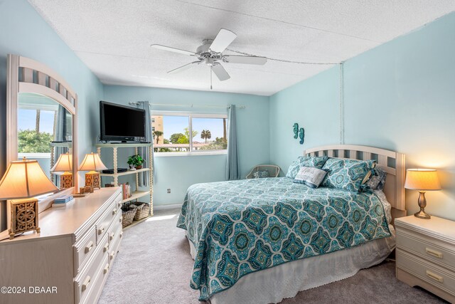 carpeted bedroom with a textured ceiling, multiple windows, and ceiling fan