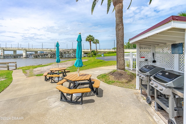 surrounding community with a dock, a lawn, a water view, and a patio area