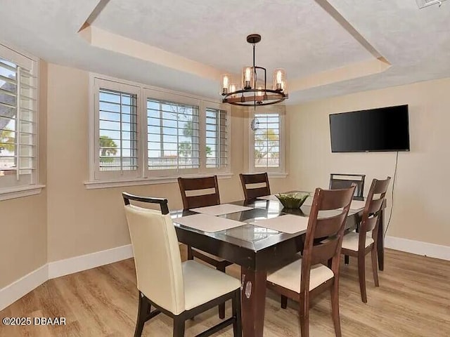 dining room with an inviting chandelier, a tray ceiling, and light hardwood / wood-style flooring