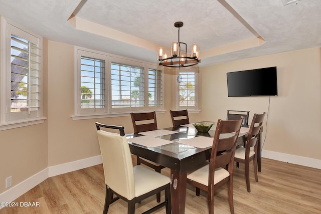 dining space with a chandelier, a raised ceiling, and light hardwood / wood-style flooring