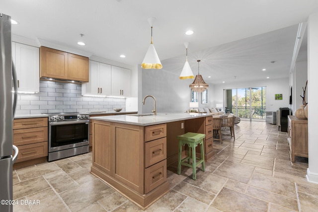 kitchen with sink, appliances with stainless steel finishes, an island with sink, white cabinets, and pendant lighting