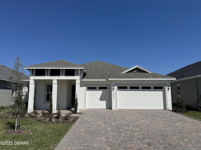 view of front of house featuring a shingled roof, decorative driveway, a garage, and stucco siding