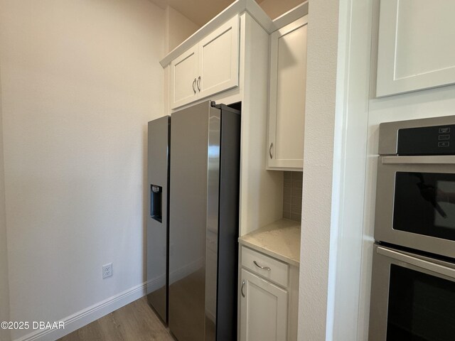 2009 Divot Dr, Daytona Beach, FL 32124 - kitchen featuring tasteful backsplash, baseboards, stainless steel appliances, light wood-style floors, and white cabinetry