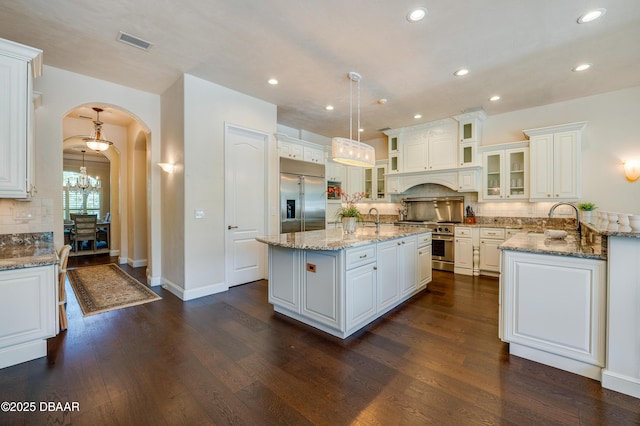 kitchen featuring a kitchen island with sink, arched walkways, decorative backsplash, a notable chandelier, and premium appliances