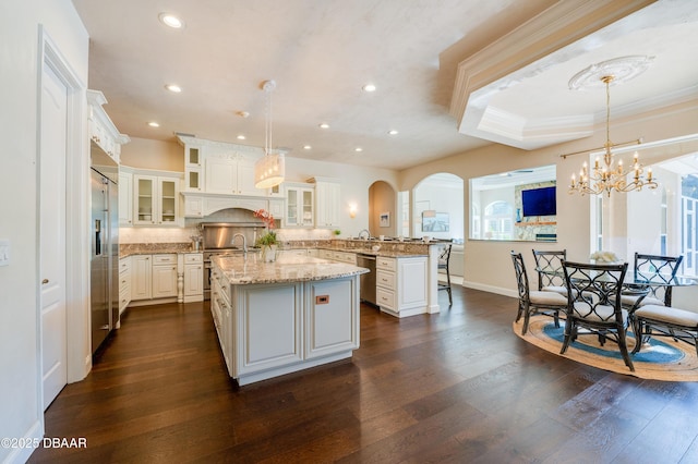 kitchen with high quality appliances, an island with sink, a peninsula, crown molding, and dark wood-style flooring